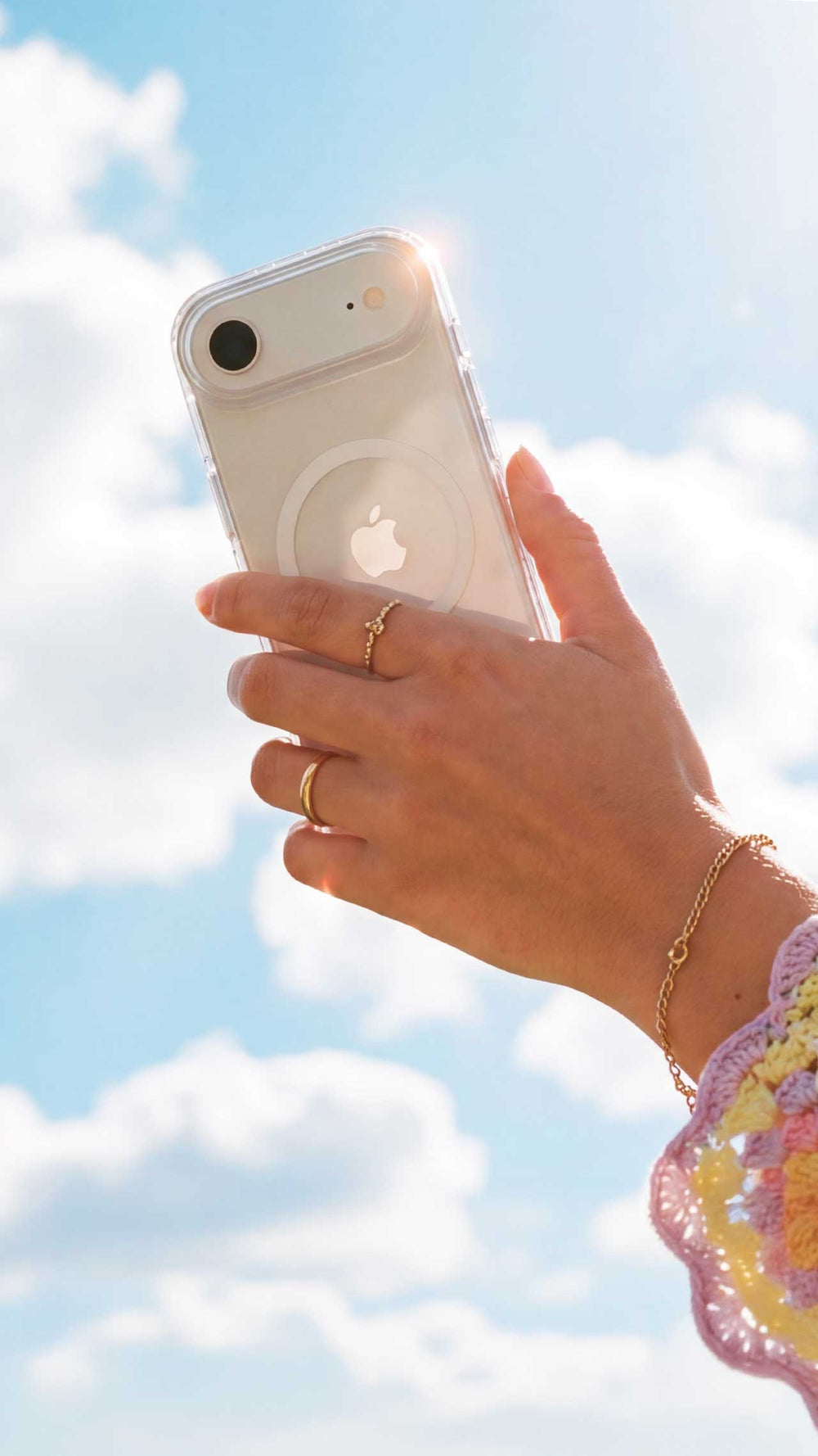 A woman's hand is shown holding an iPhone in a clear case by Tech21 with a blue sky and patchy clouds in the background